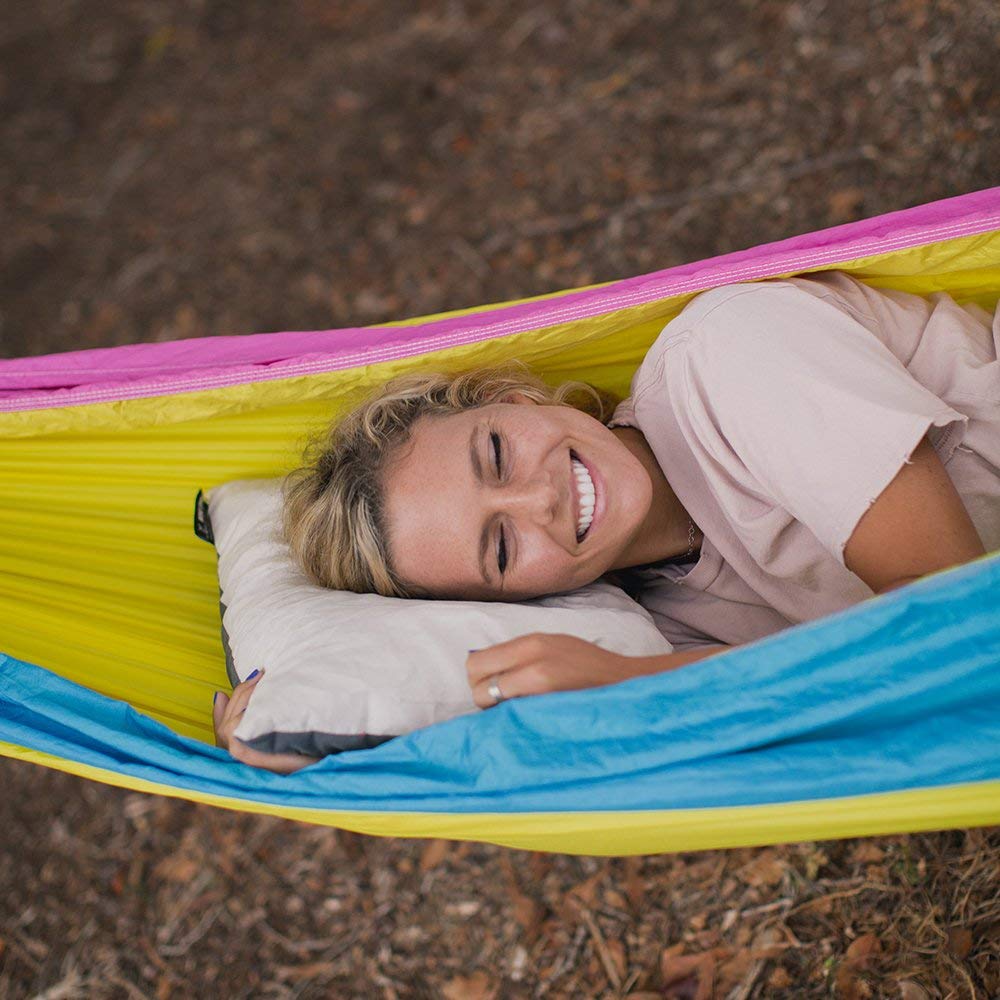 Women in a hammock laying on a camping pillow outside in the woods.