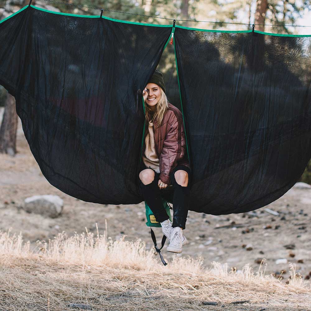 Women using a hammock bug net while sitting in a hammock.