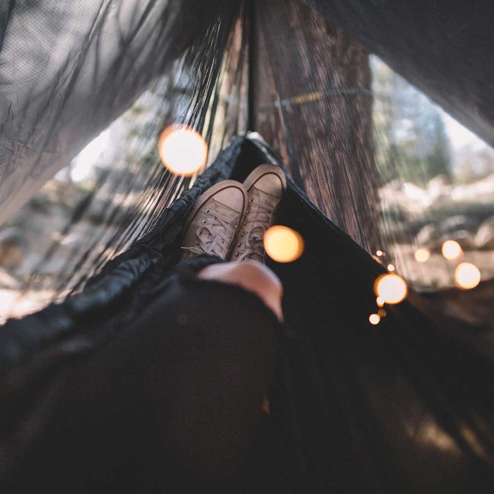Women using a hammock outside with a hammock bug net in the woods.