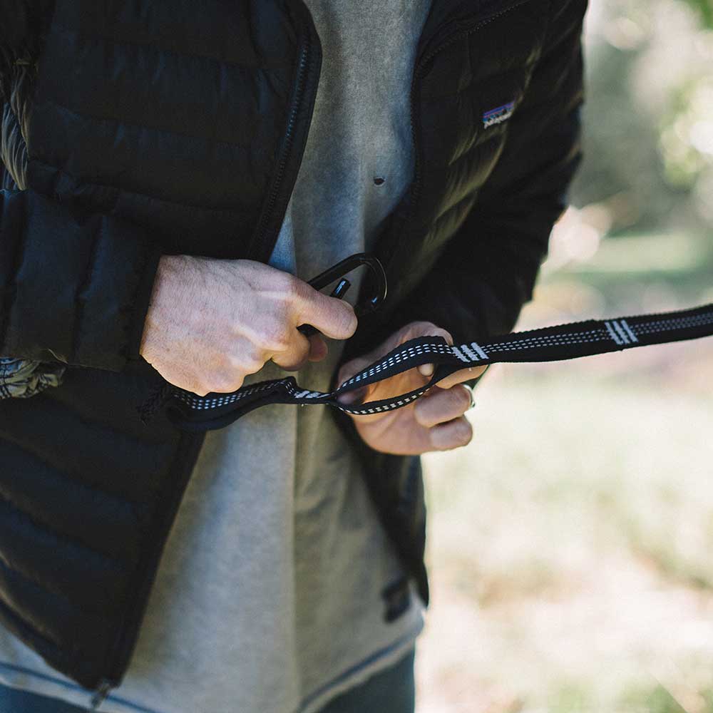 Man securing hammock straps around a tree using hammock hooks.