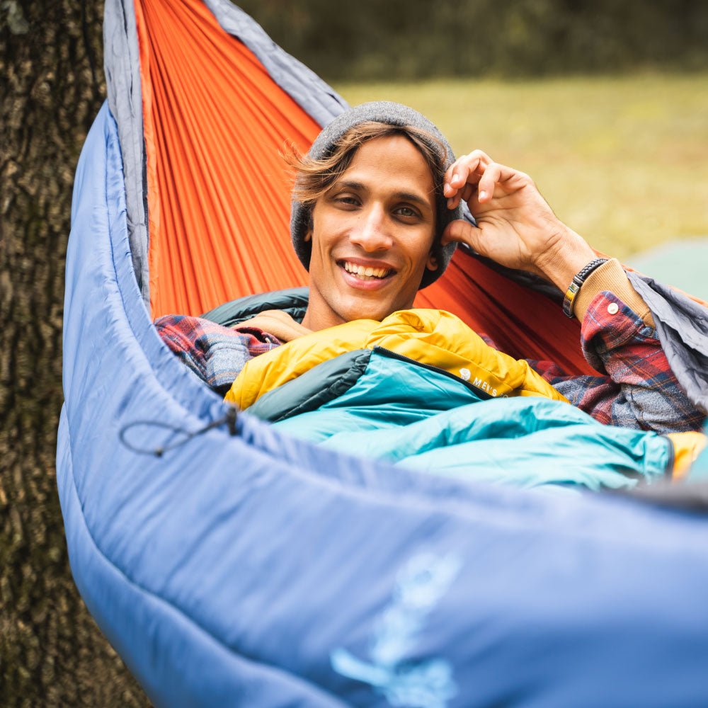 Man smiling using our blue hammock underquilt outdoors.