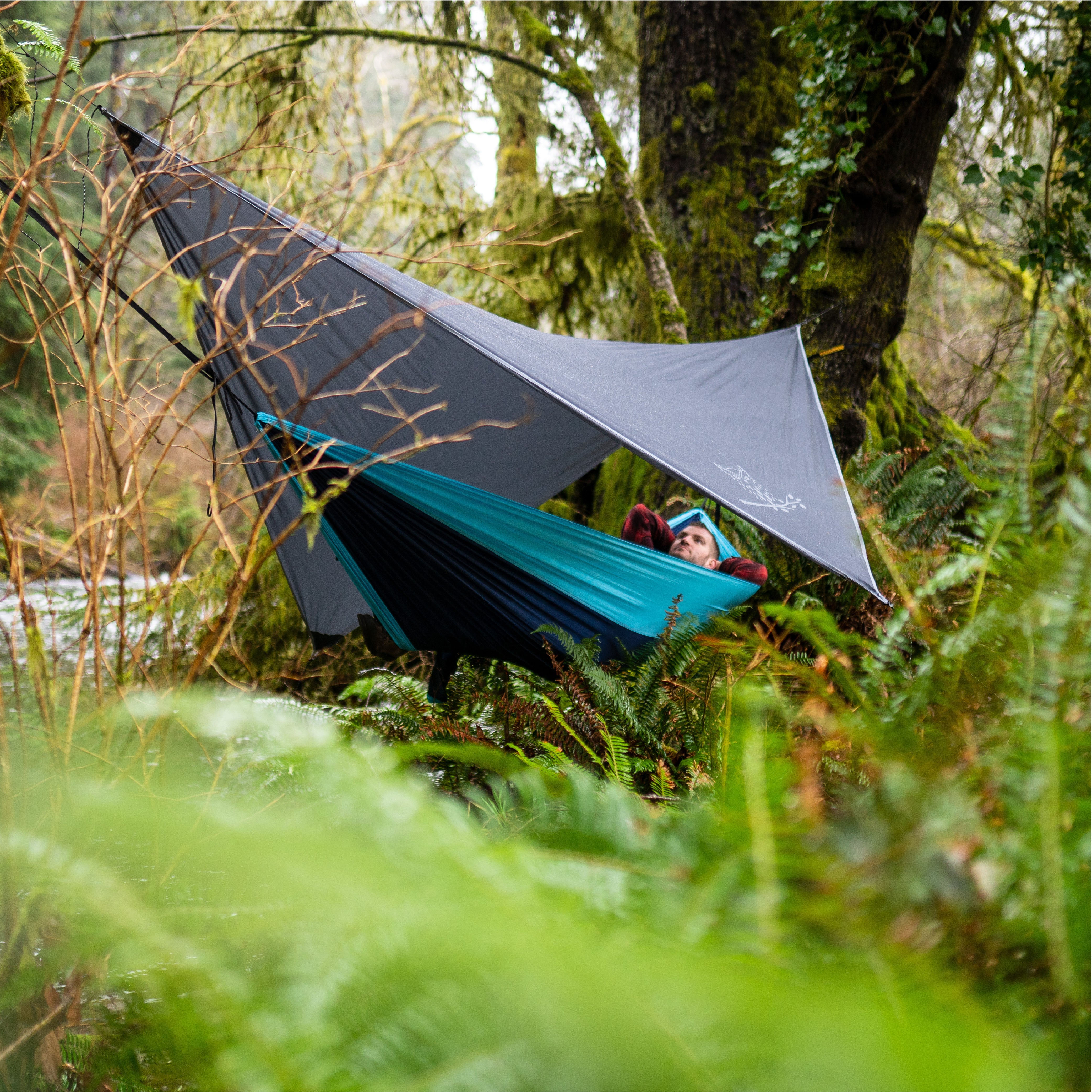 Man using a waterproof hammock tarp in the woods while hiking.