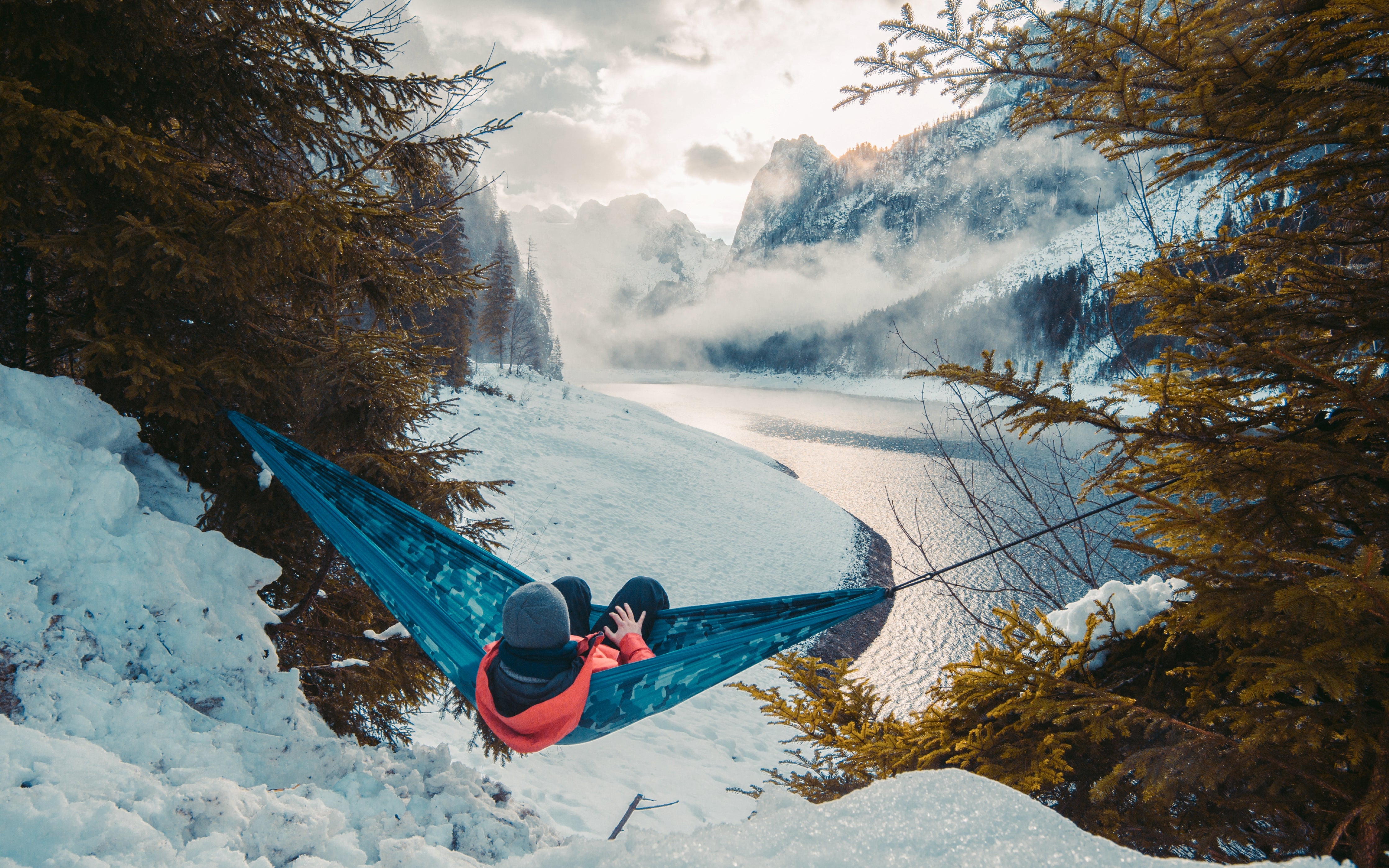 man in hammock camping in winter with beautiful view of lake and mountains 