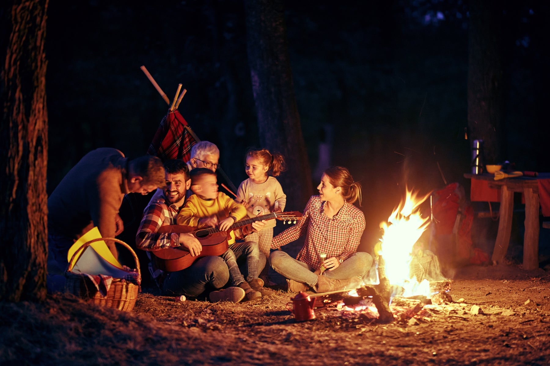 family enjoying some outdoor night activities for kids by a campfire roasting marshmallows