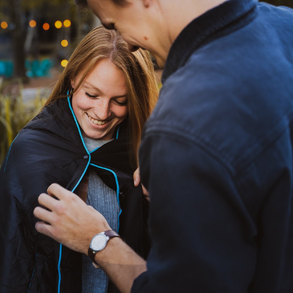 Man helping women clasp a camping blanket closed to keep her warm.