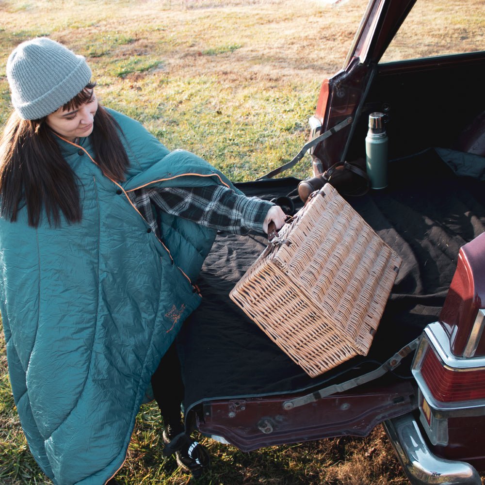 Women grabbing a picnic basket outside while using a camping blanket.