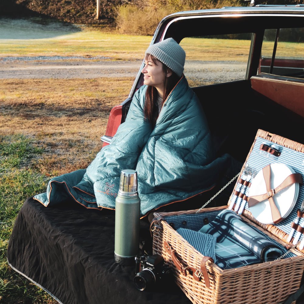 Women using a camping blanket at a picnic outside to warm up.