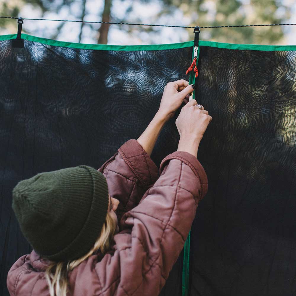 Women unzipping a hammock bug net outside.