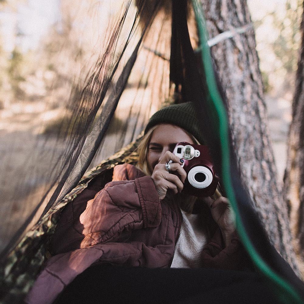 Women using a camera in a hammock with a hammock bug net.