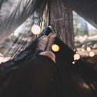 Women using a hammock outside with a hammock bug net in the woods.