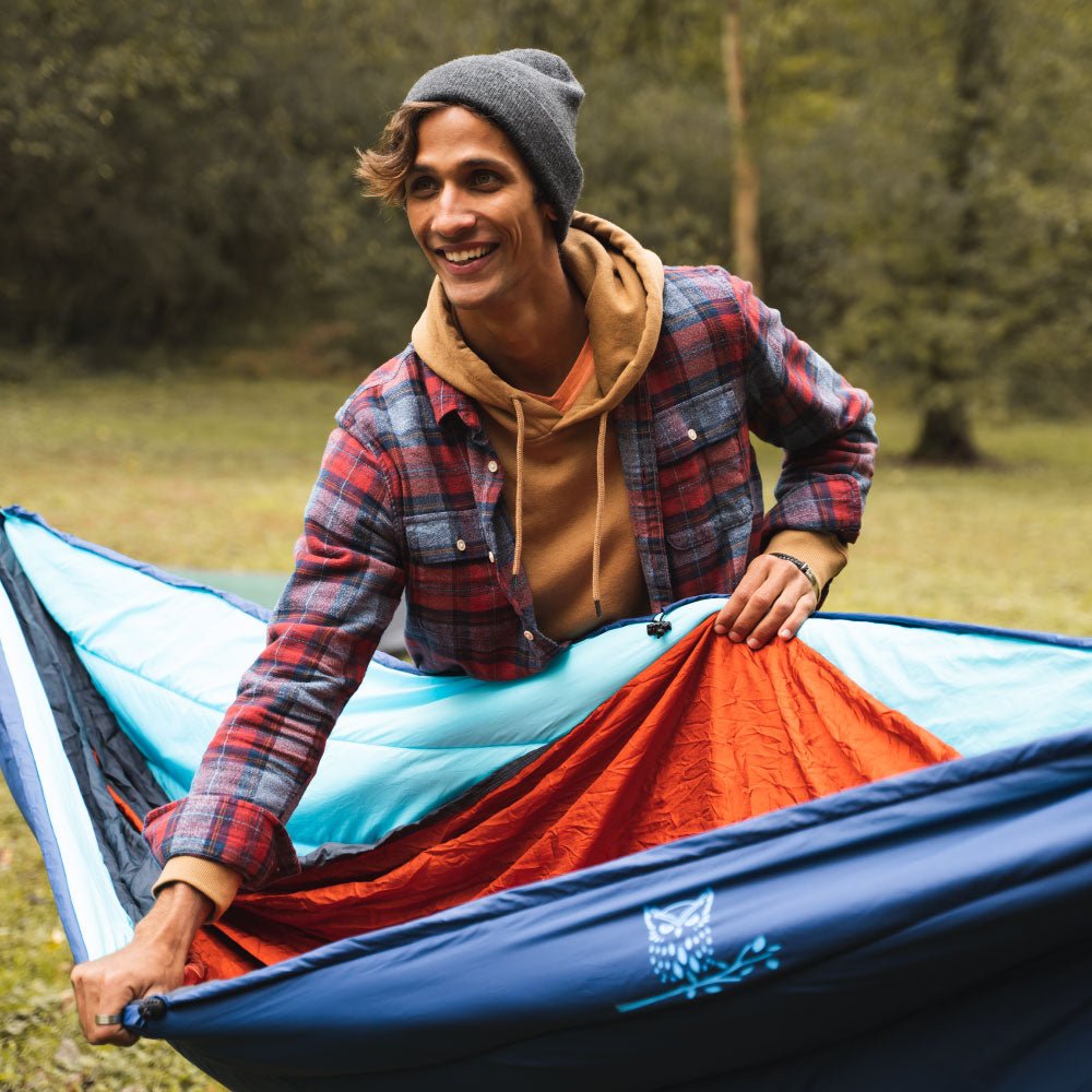 Man opening underquilt outdoors to stay warm.