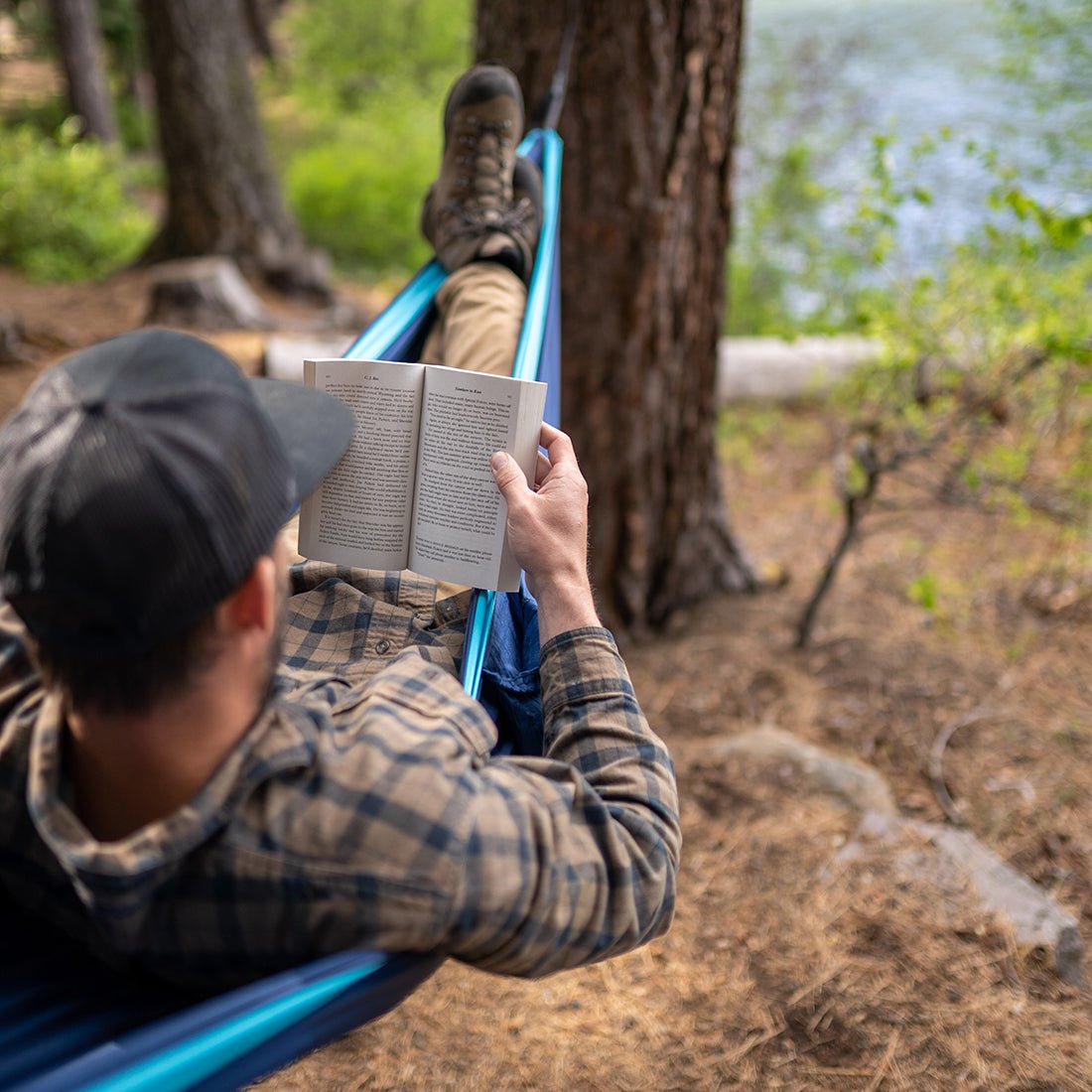 Man reading a book in a camping hammock outdoors. 
