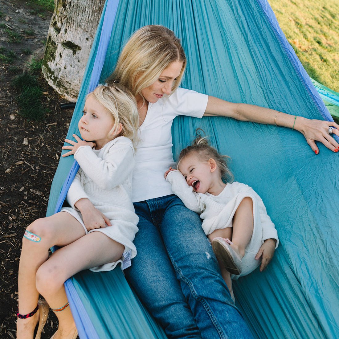A woman and her children laying in a two person hammock outside. 