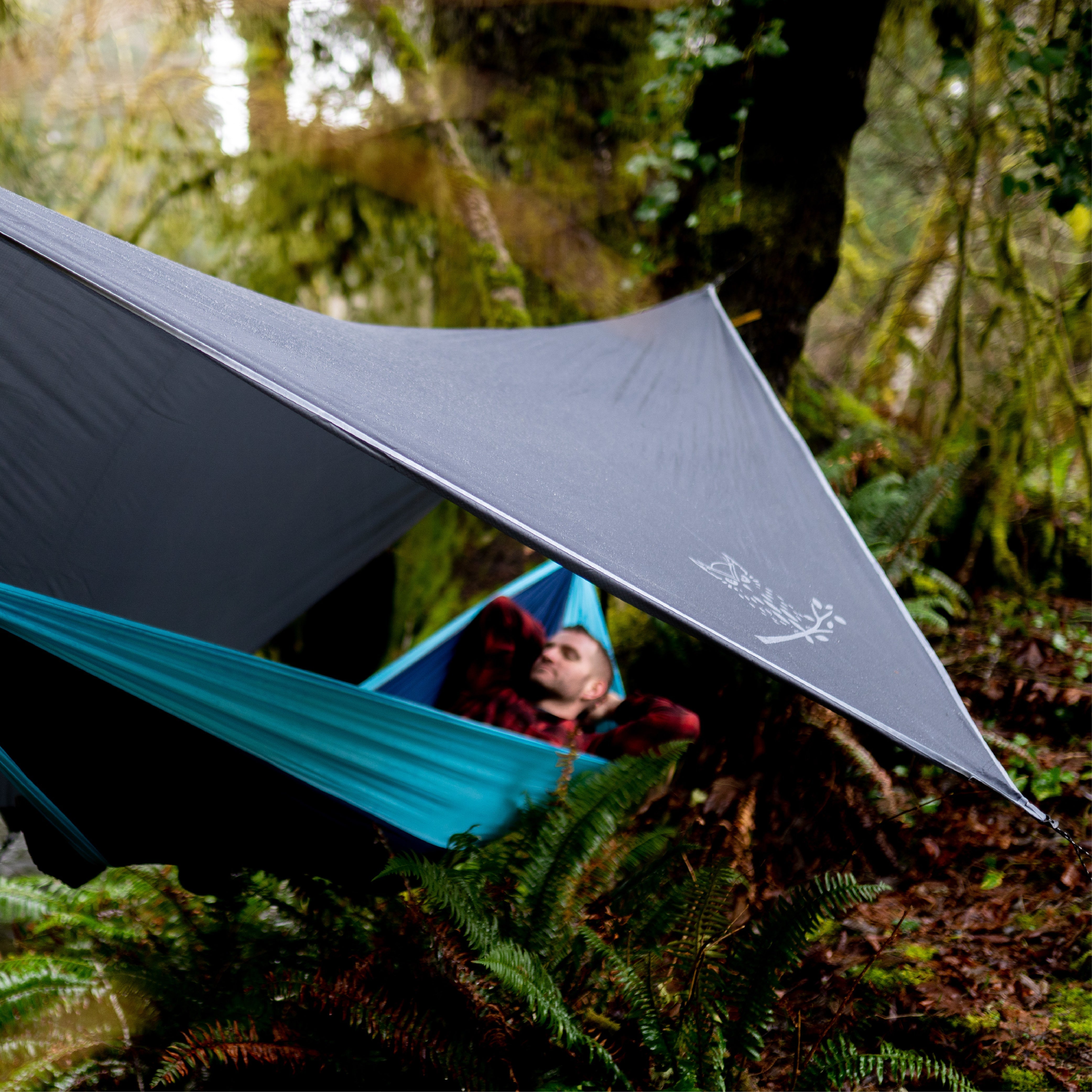 Man laying in a camping hammock with a waterproof hammock tarp.
